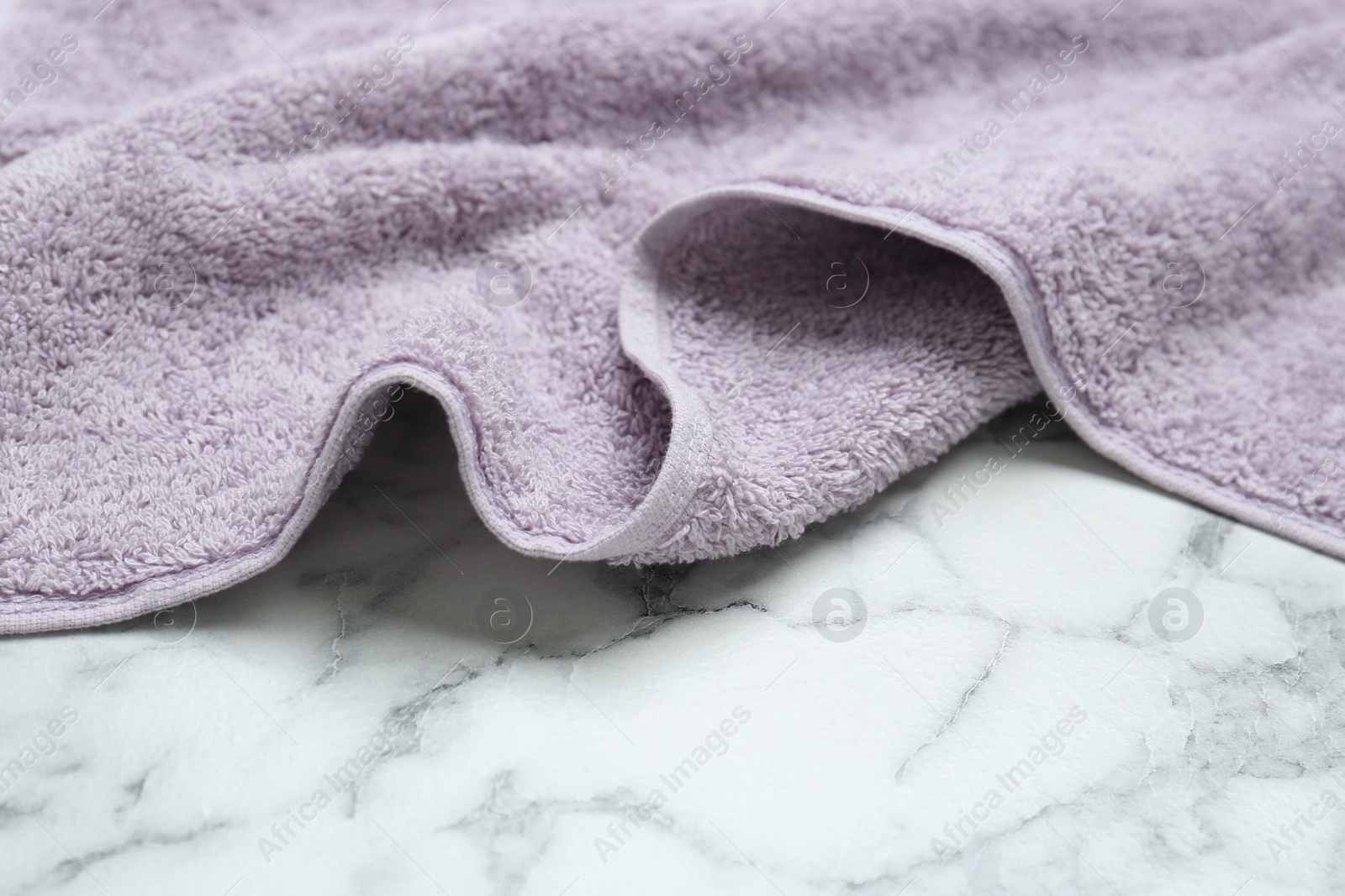 Photo of Violet terry towel on white marble table. Space for text