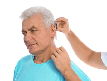 Young man putting hearing aid in father's ear on white background