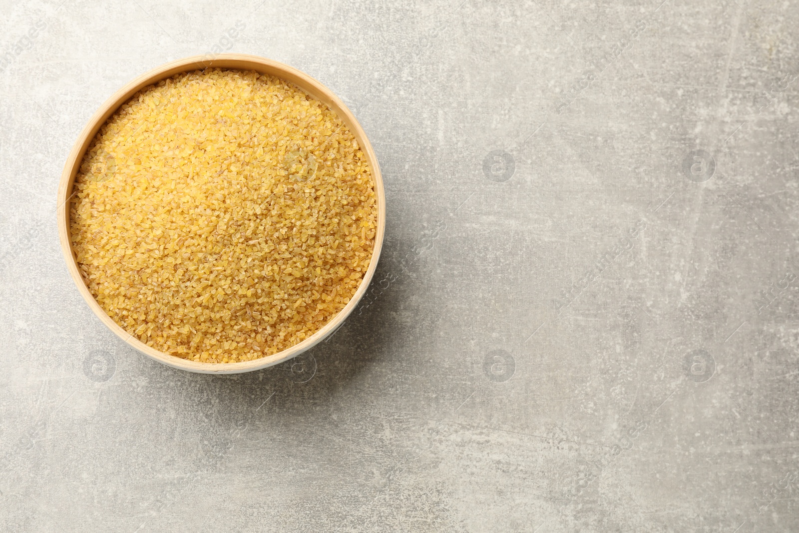 Photo of Raw bulgur in bowl on gray table, top view. Space for text