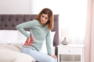Woman suffering from back pain on bed at home