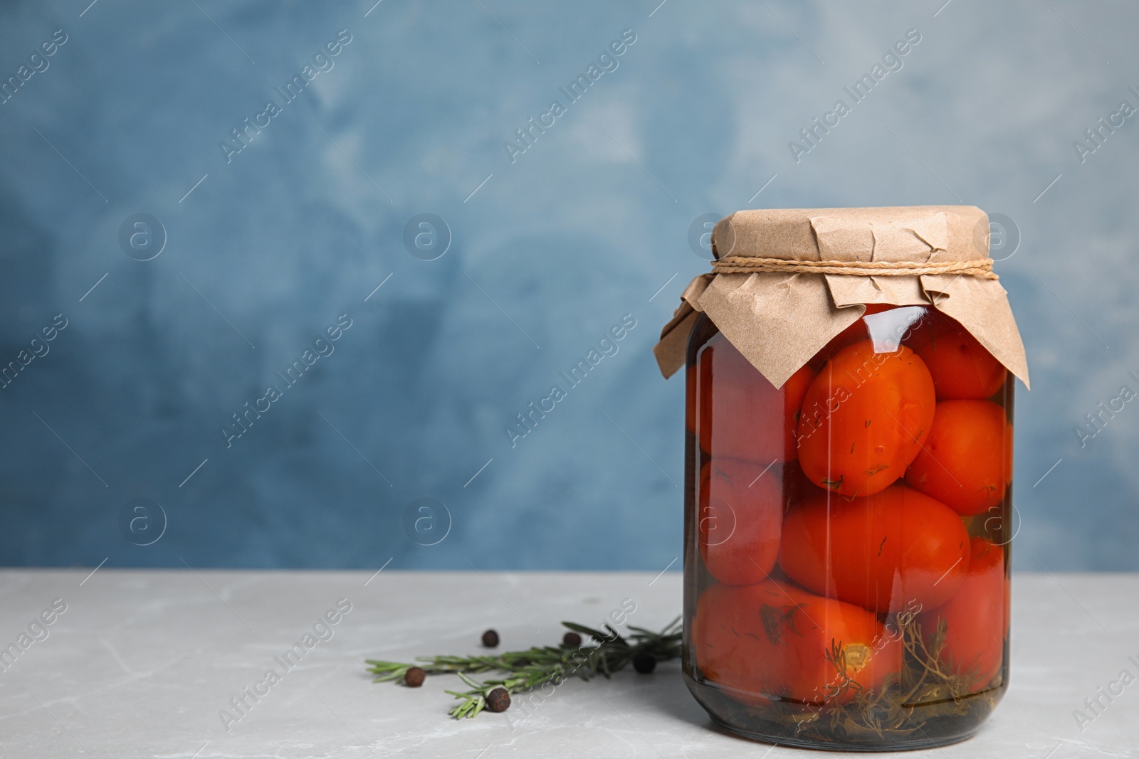Photo of Pickled tomatoes in glass jar on grey table against blue background, space for text