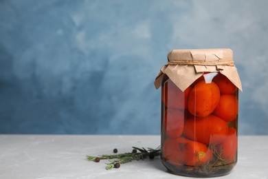 Pickled tomatoes in glass jar on grey table against blue background, space for text