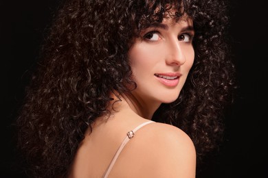 Photo of Beautiful young woman with long curly hair on black background, closeup