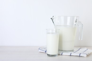 Photo of Jug and glass of fresh milk on wooden table, space for text