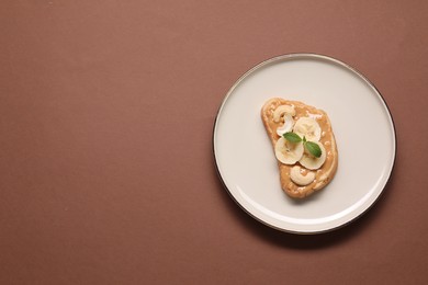Photo of Toast with tasty nut butter, banana slices and cashews on brown background, top view. Space for text
