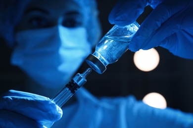 Photo of Woman filling syringe with vaccine from vial on black background, closeup
