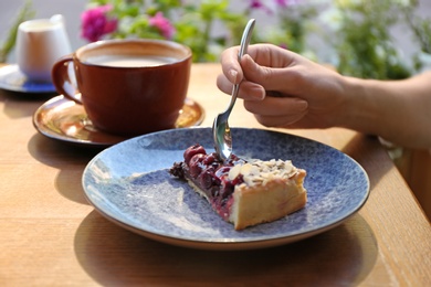 Photo of Woman eating slice of cherry cake at table, closeup