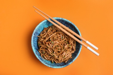 Photo of Bowl of buckwheat noodles with chopsticks on color background, top view