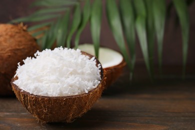 Photo of Coconut flakes in nut shell on wooden table, space for text