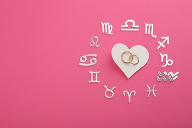 Zodiac signs, heart and wedding rings on pink background, flat lay. Space for text