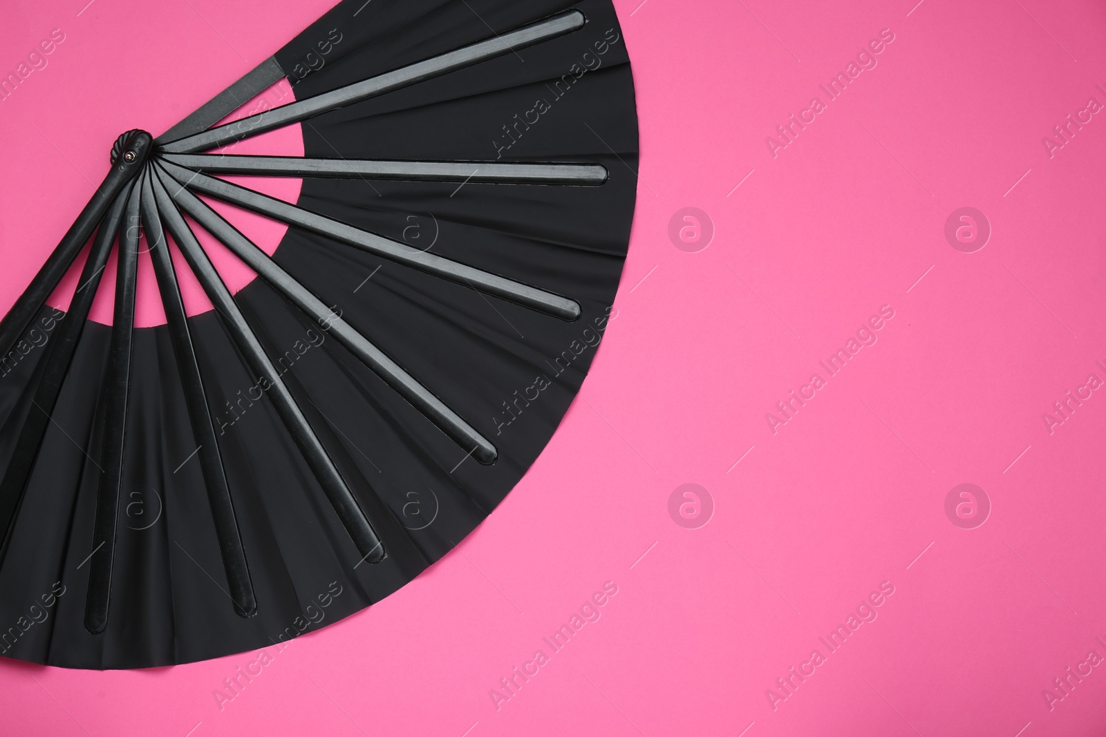 Photo of Stylish black hand fan on pink background, top view. Space for text