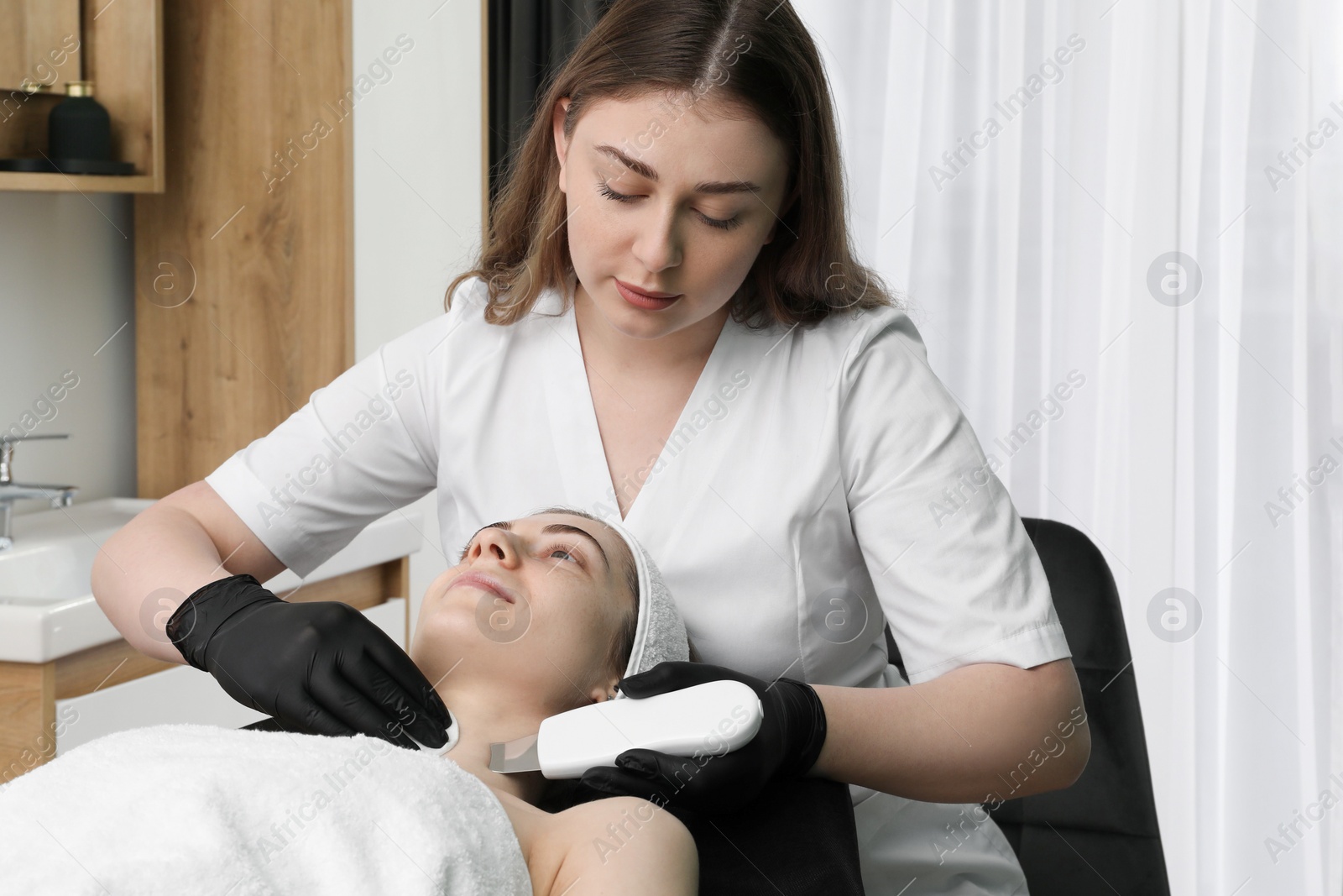 Photo of Cosmetologist using ultrasonic scrubber. Client having cleansing procedure in clinic