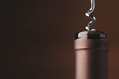 Image of Opening bottle of wine with corkscrew on brown background, closeup. Space for text