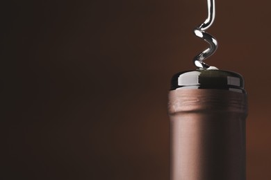 Opening bottle of wine with corkscrew on brown background, closeup. Space for text