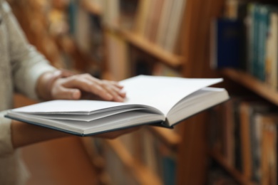 Photo of Woman holding open book in library, closeup