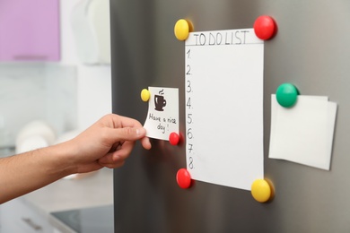 Man putting paper sheet on refrigerator door at home, closeup