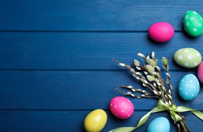Photo of Bright painted eggs and pussy willows on blue wooden table, flat lay with space for text. Happy Easter