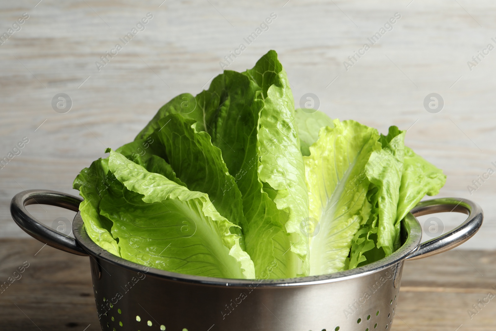 Photo of Colander with fresh leaves of green romaine lettuce on wooden background, closeup