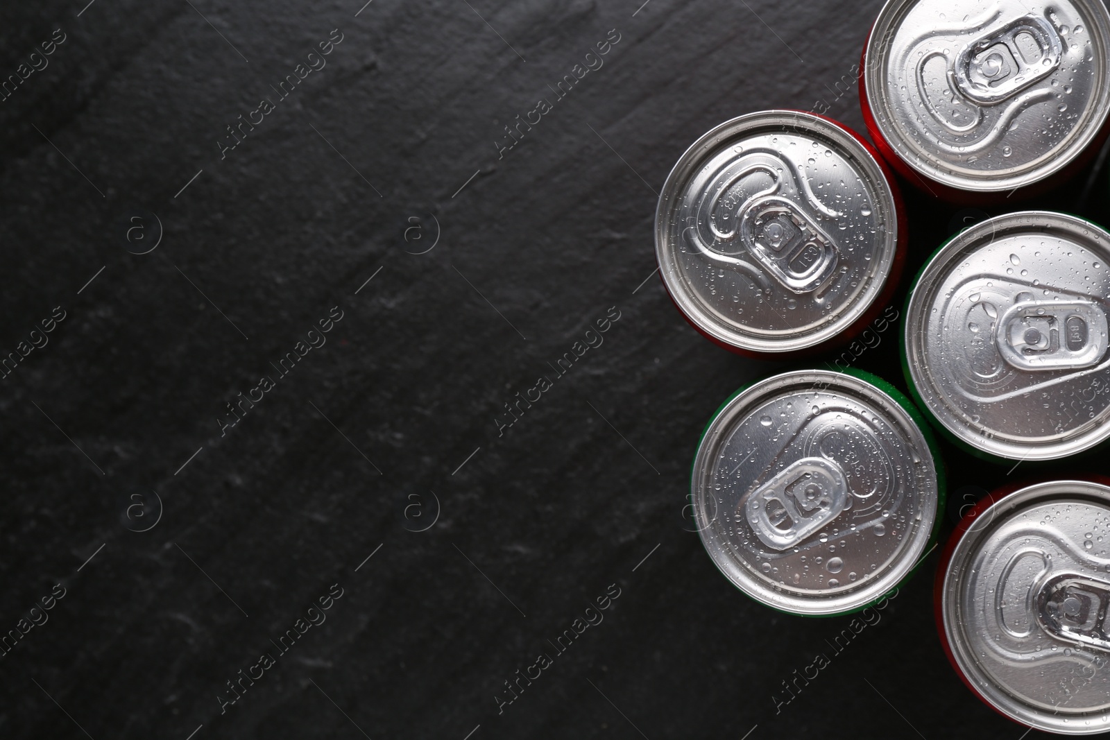 Photo of Energy drink in wet cans on black textured background, top view. Space for text