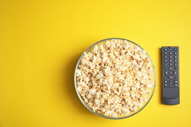 Bowl of popcorn, TV remote and space for text on color background, top view. Watching cinema