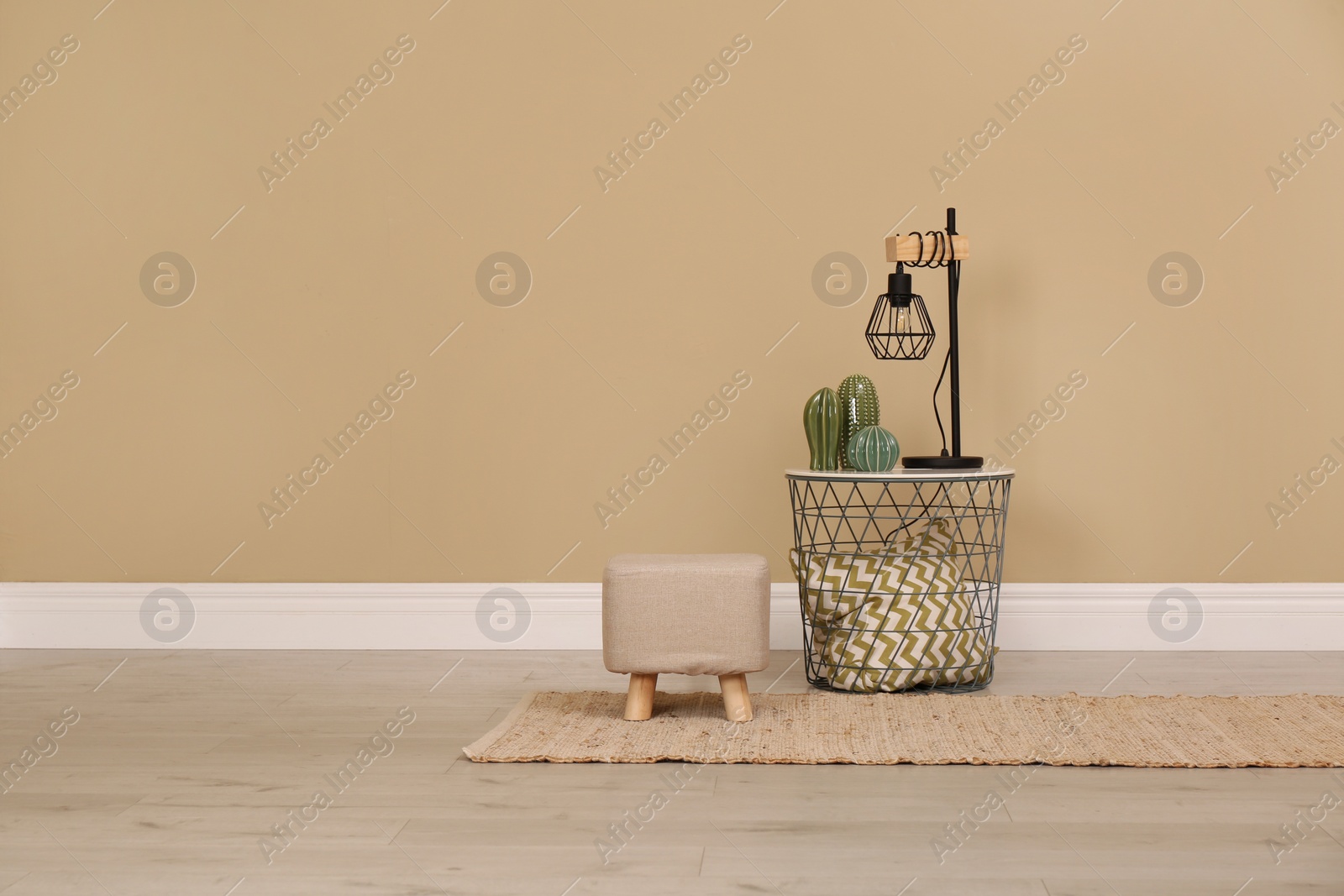 Photo of Stylish comfortable ottoman and lamp near beige wall indoors, space for text