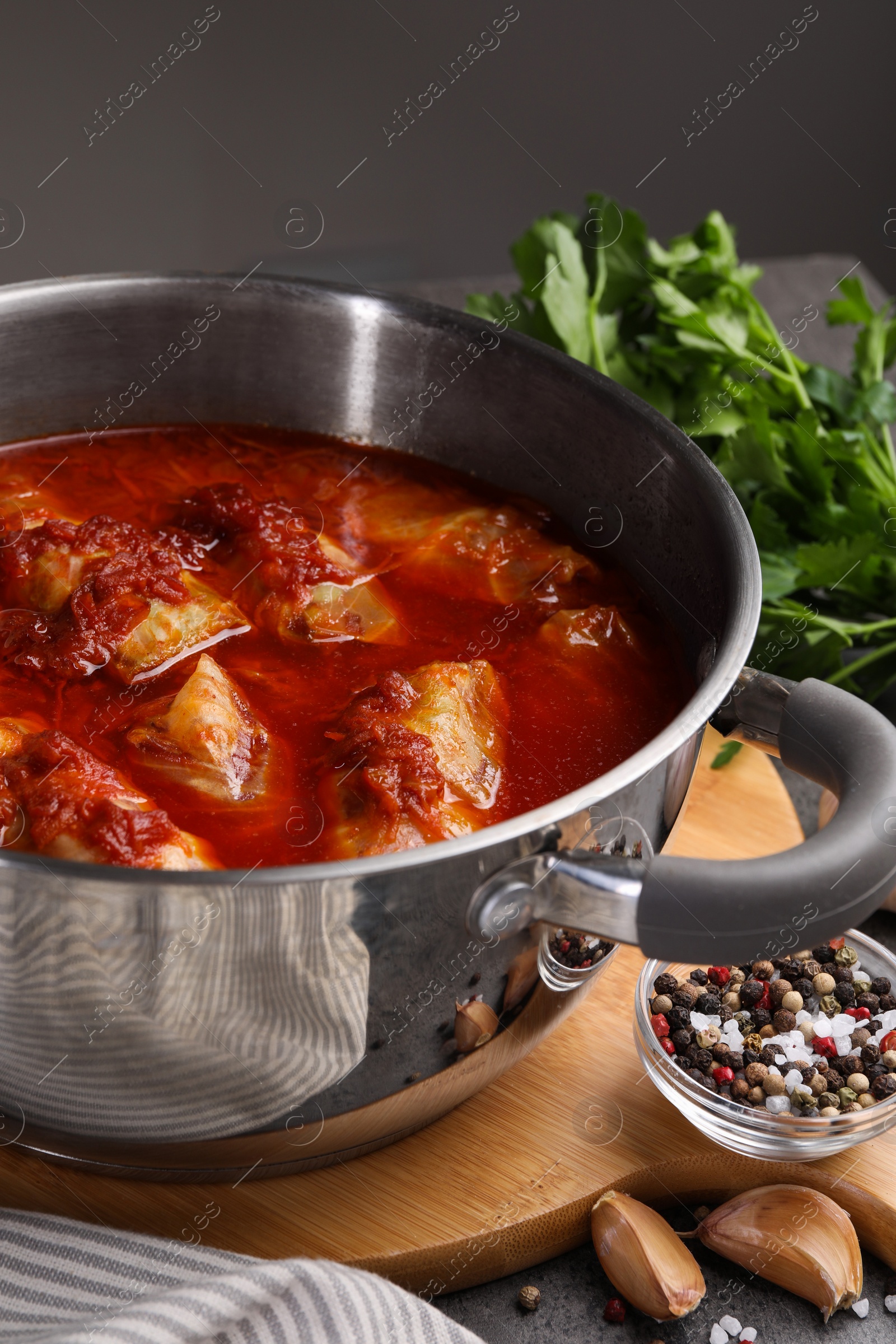 Photo of Delicious stuffed cabbage rolls cooked with homemade tomato sauce in pot and ingredients on table, closeup