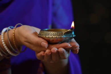 Photo of Woman holding lit diya lamp in hands on dark background, closeup. Diwali celebration