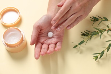 Photo of Woman applying cosmetic cream onto hand on beige background, above view