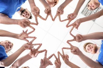 Team of volunteers putting their hands together on light background, bottom view