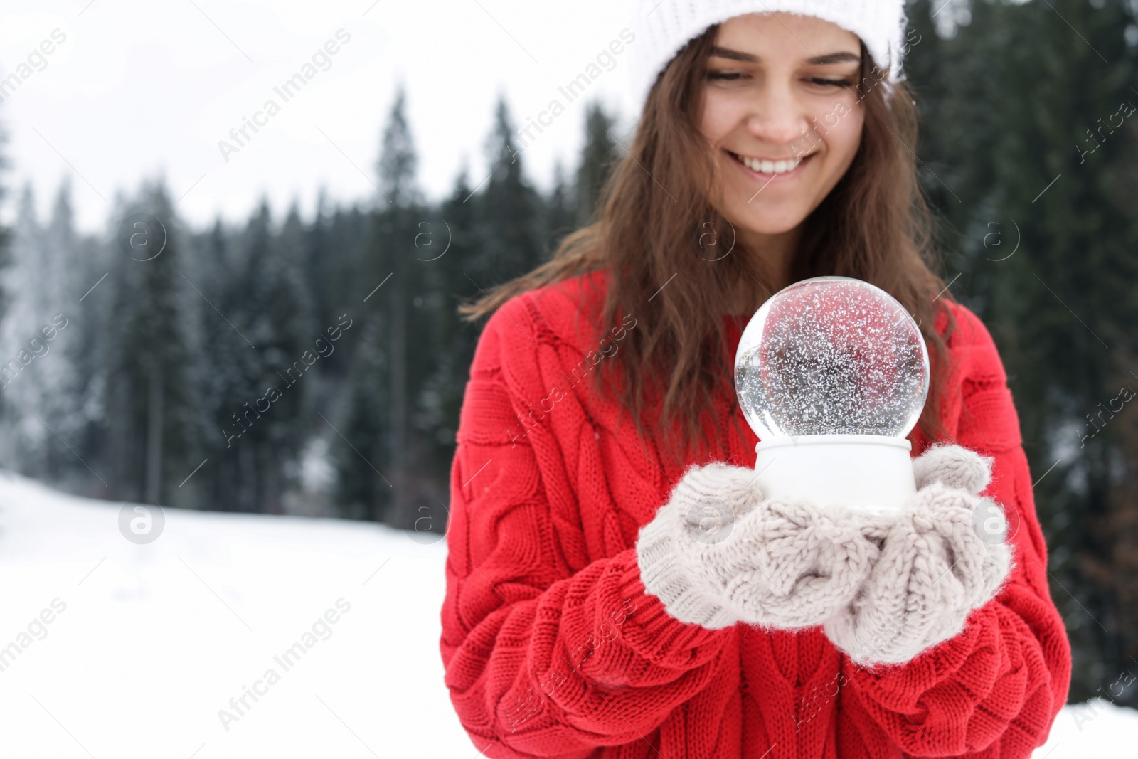 Photo of Young woman in knitted clothes holding snow globe outdoors, space for text. Winter vacation