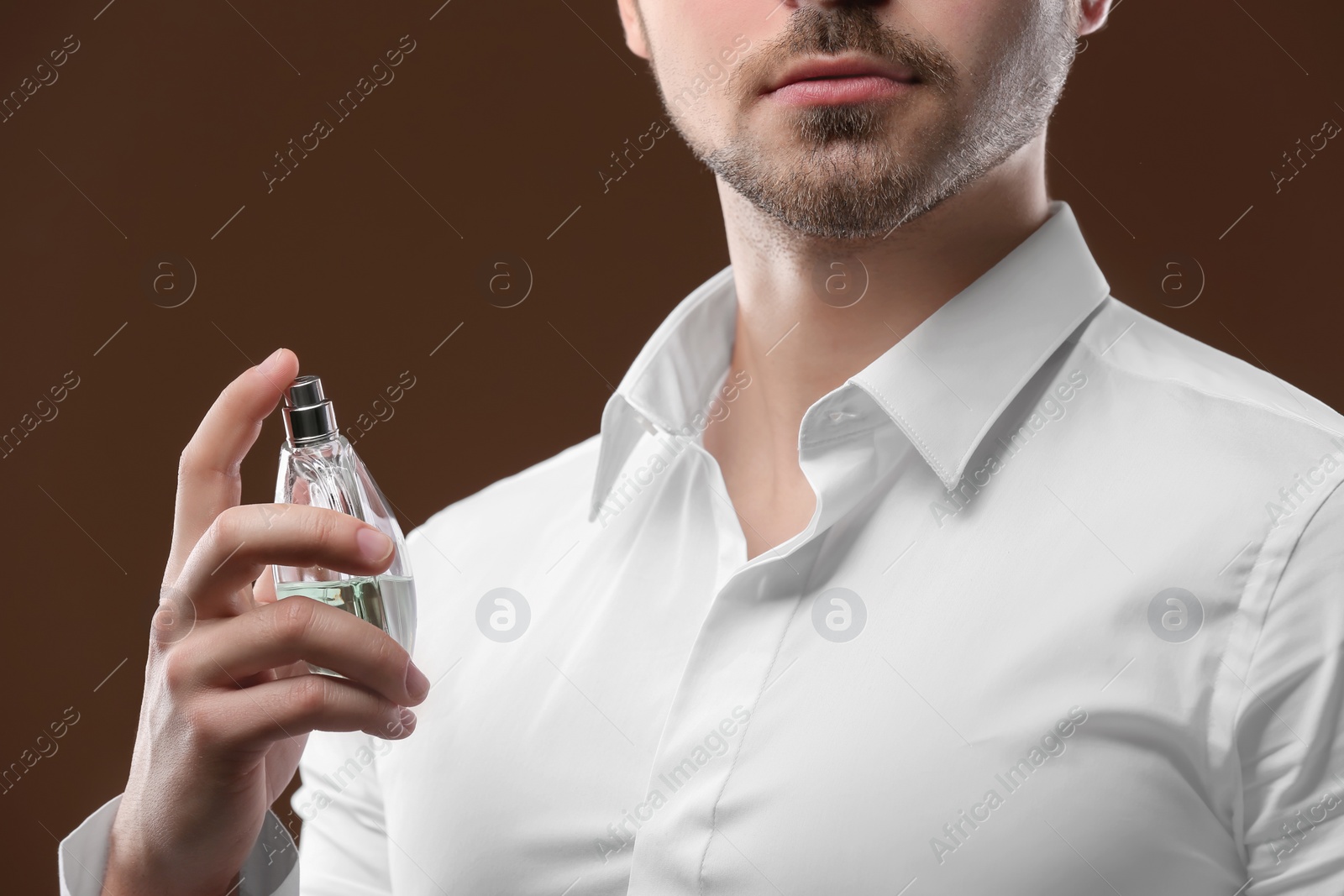 Photo of Handsome man in shirt using perfume on dark background, closeup