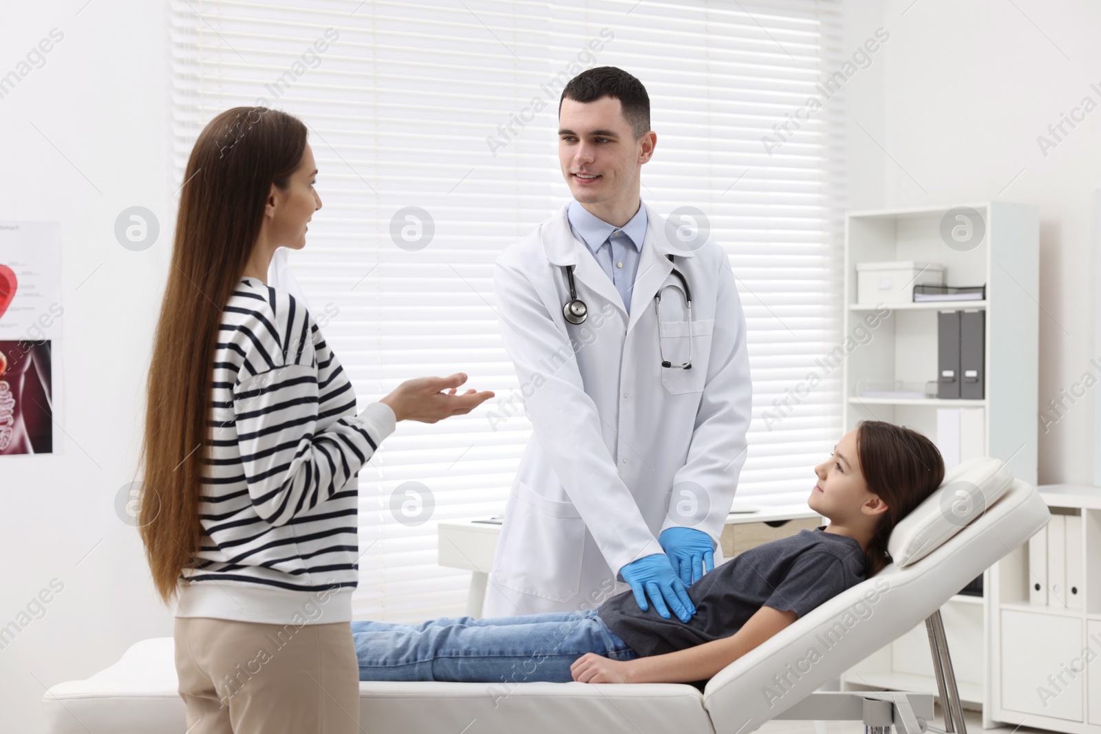 Photo of Gastroenterologist examining girl with stomach ache on couch in clinic