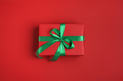 Photo of Christmas gift box with green ribbon on red background, top view