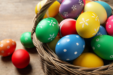 Photo of Colorful Easter eggs in basket on wooden background, closeup