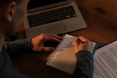 Man taking notes at wooden table in evening, closeup