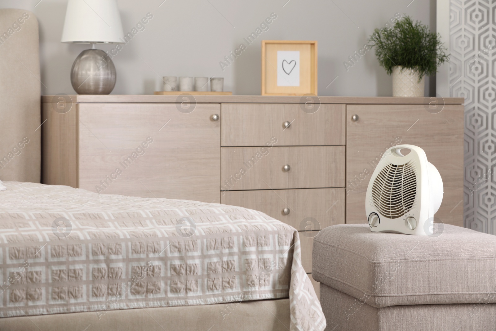 Photo of Modern electric fan heater on pouf in cozy room