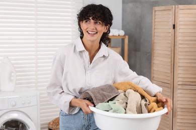Photo of Happy woman holding basin with laundry indoors