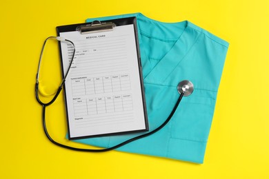 Medical uniform, stethoscope and clipboard on yellow background, flat lay