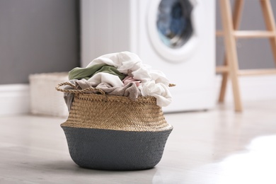 Photo of Wicker basket with dirty laundry on floor indoors, space for text