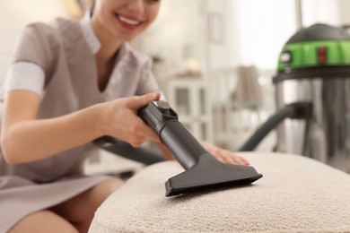 Photo of Professional chambermaid vacuuming pouf indoors, closeup. Cleaning service