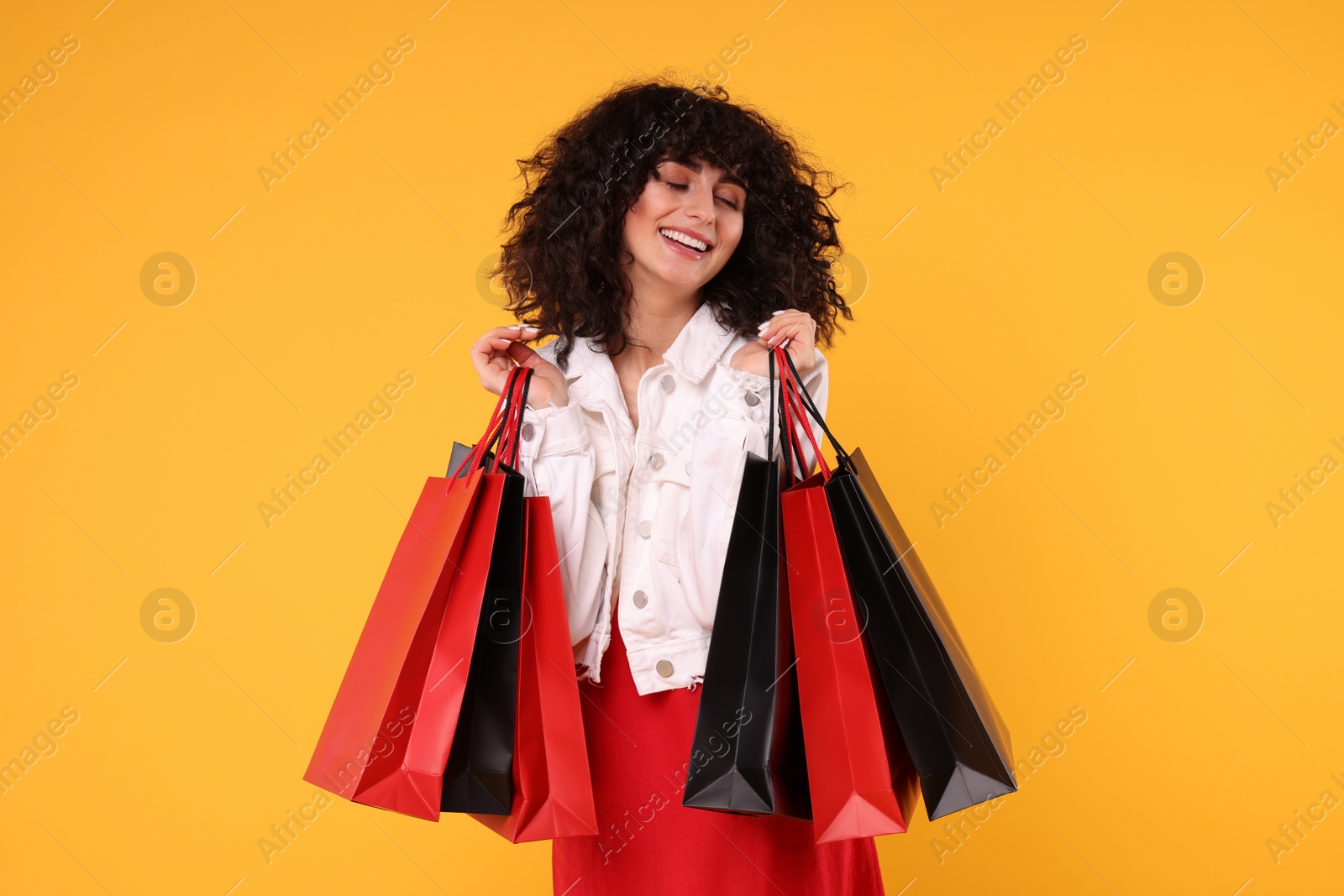 Photo of Happy young woman with shopping bags on yellow background