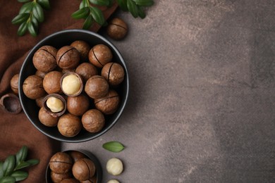 Tasty Macadamia nuts and green twigs on brown table, flat lay. Space for text