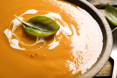 Photo of Tasty creamy pumpkin soup with basil in bowl, closeup