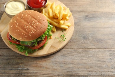 Photo of Delicious burger with beef patty, sauce and french fries on wooden table, above view. Space for text