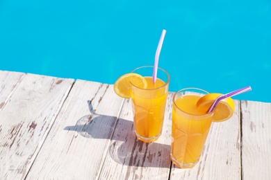 Photo of Refreshing cocktails near outdoor swimming pool on sunny day. Space for text