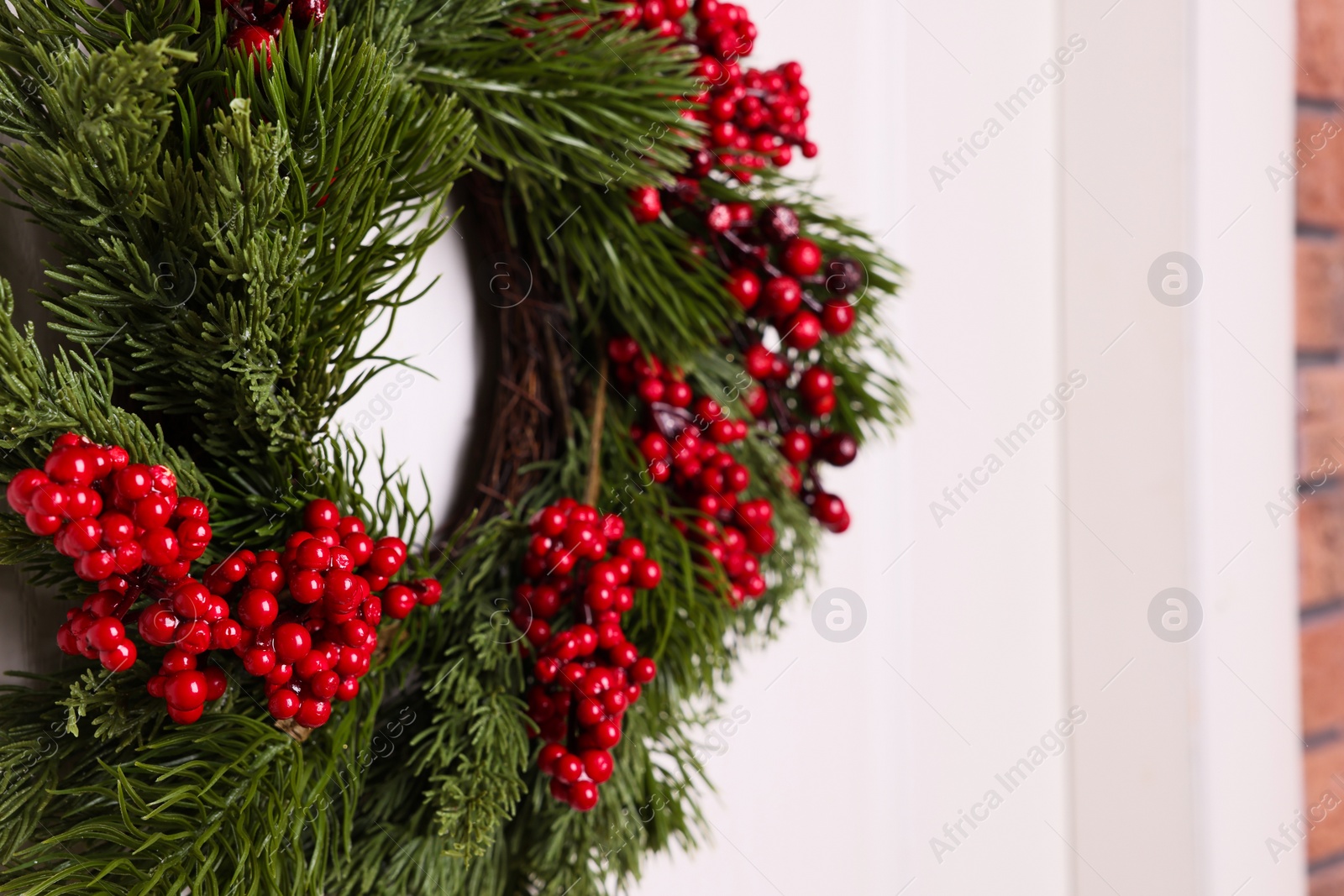 Photo of Beautiful Christmas wreath with red berries hanging on white door, closeup. Space for text