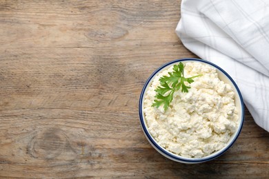 Delicious fresh cottage cheese with parsley on wooden table, flat lay. Space for text