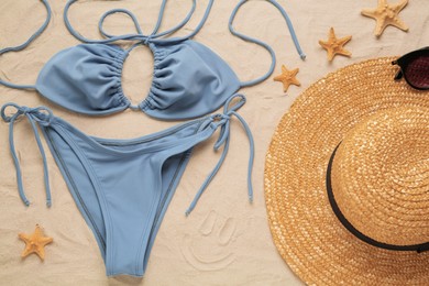 Stylish bikini, straw hat, sunglasses and starfishes on sand, flat lay