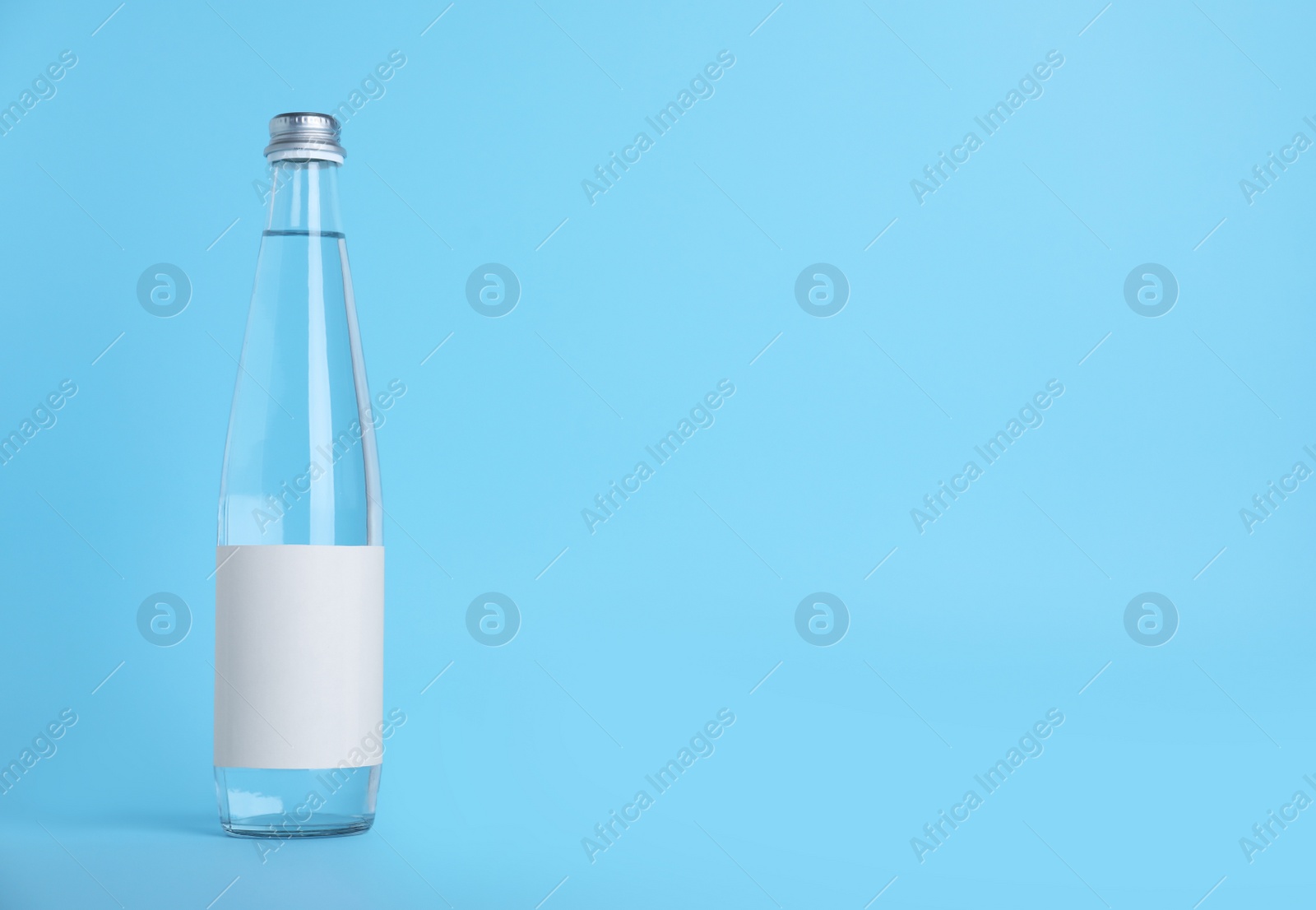 Photo of Glass bottle with soda water on light blue background. Space for text
