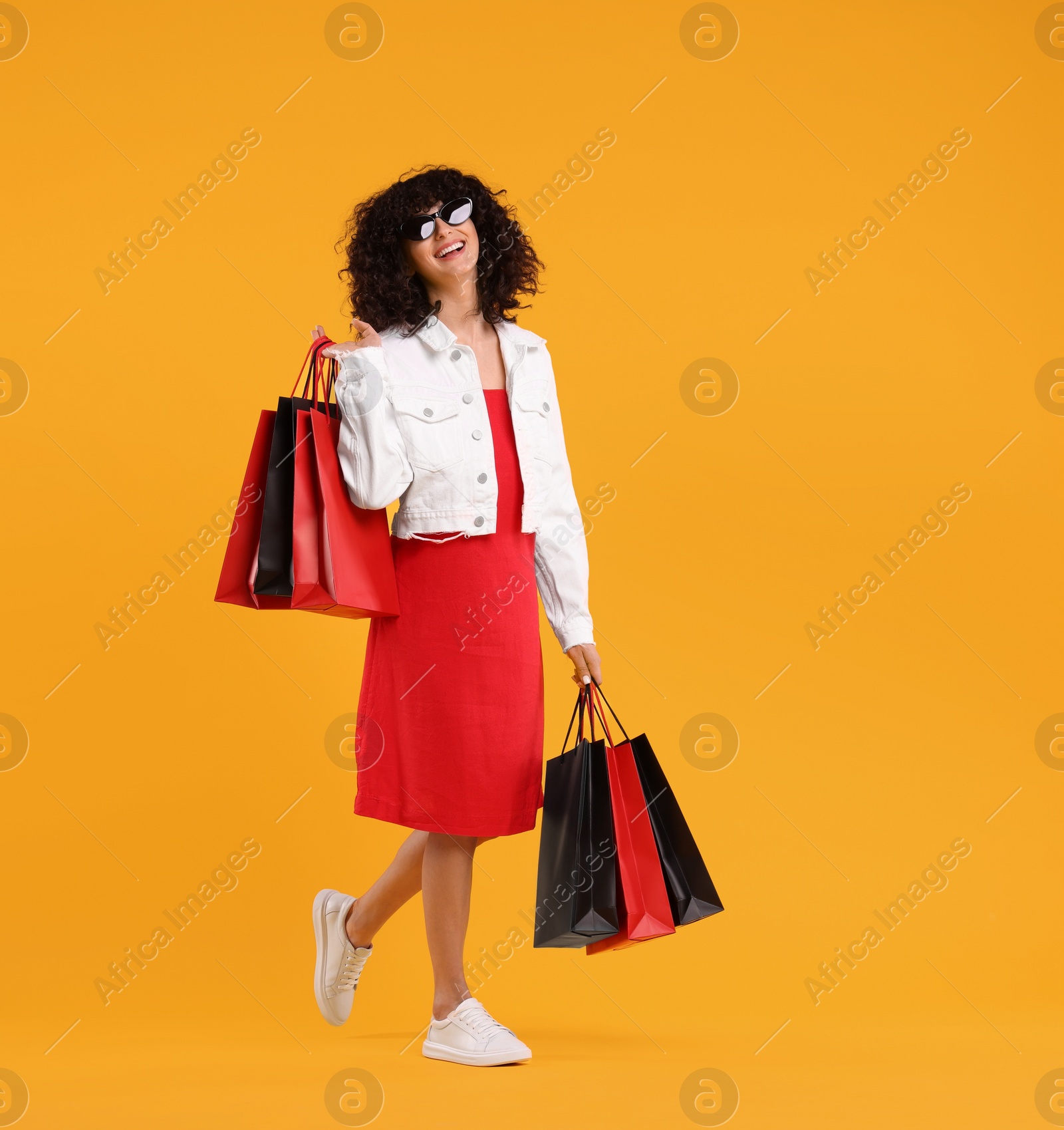 Photo of Happy young woman with shopping bags and stylish sunglasses on yellow background. Space for text